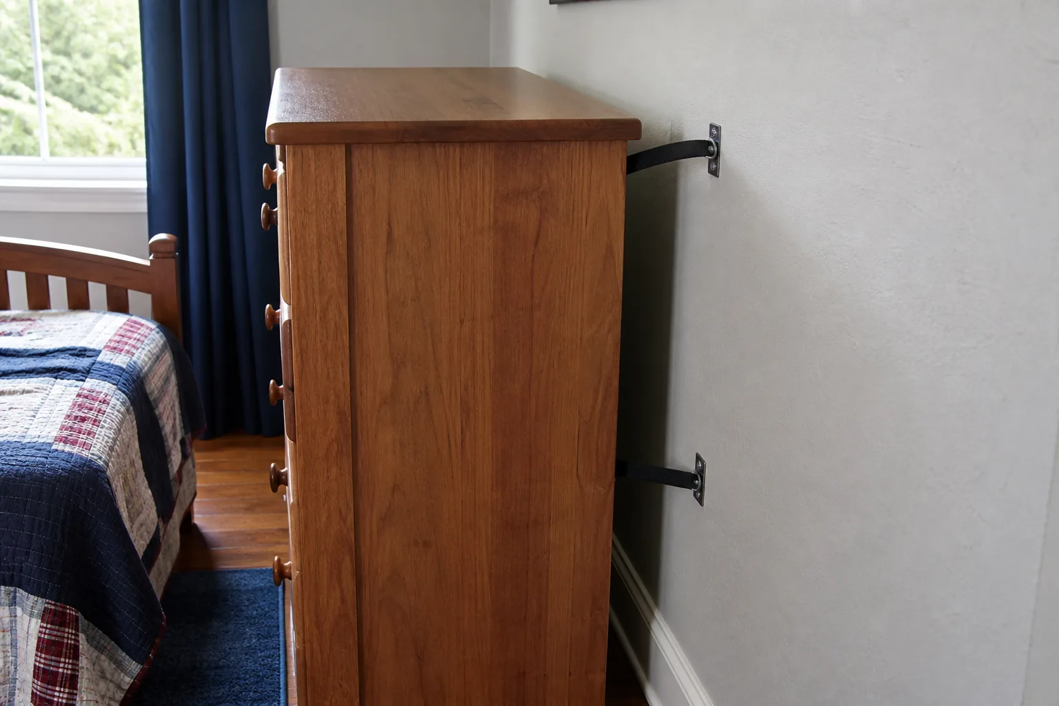 Tall wood dresser secured to the wall with two visible anti-tip straps