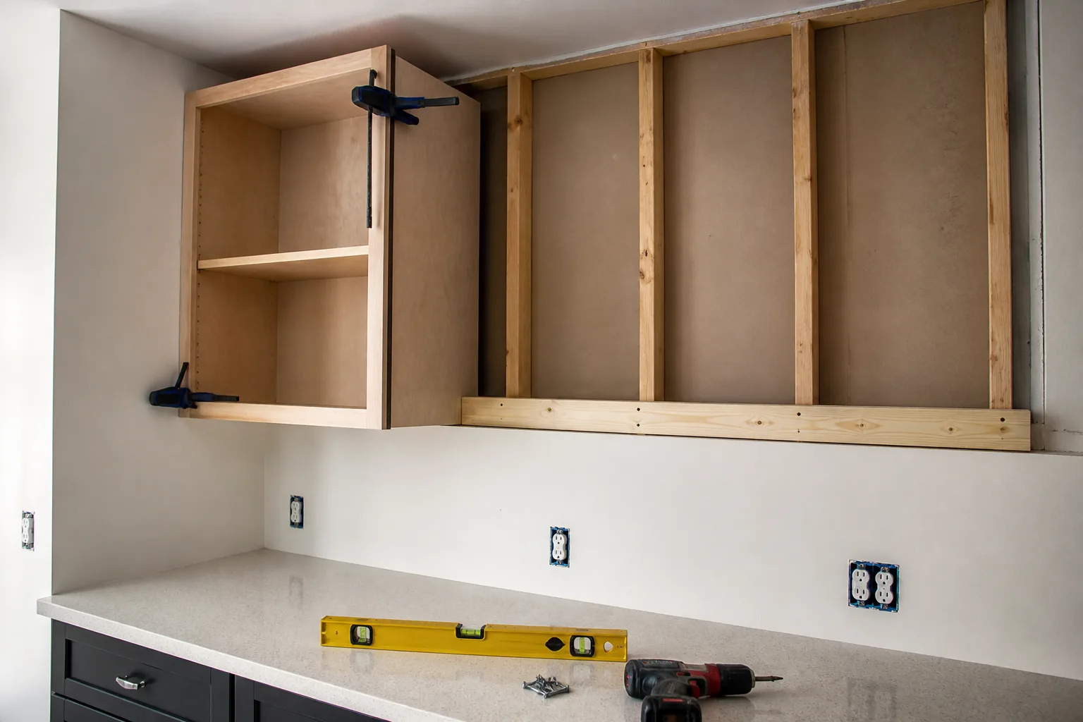 Upper kitchen cabinet supported on a ledger beside exposed wood wall studs